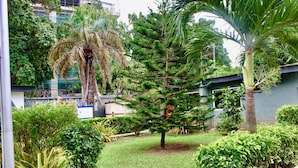 Un jardin bien entretenu, agrémenté de divers arbres et arbustes, avec un chemin dégagé et un bâtiment visible au loin.