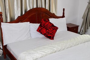 A bed with white linens, a red patterned pillow, and a wooden headboard. - The Residence Apartments (Lagos)