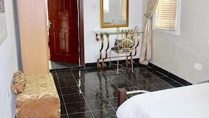 Une chambre à coucher avec un lit, une porte en bois, une table en verre avec une chaise et un miroir au mur.