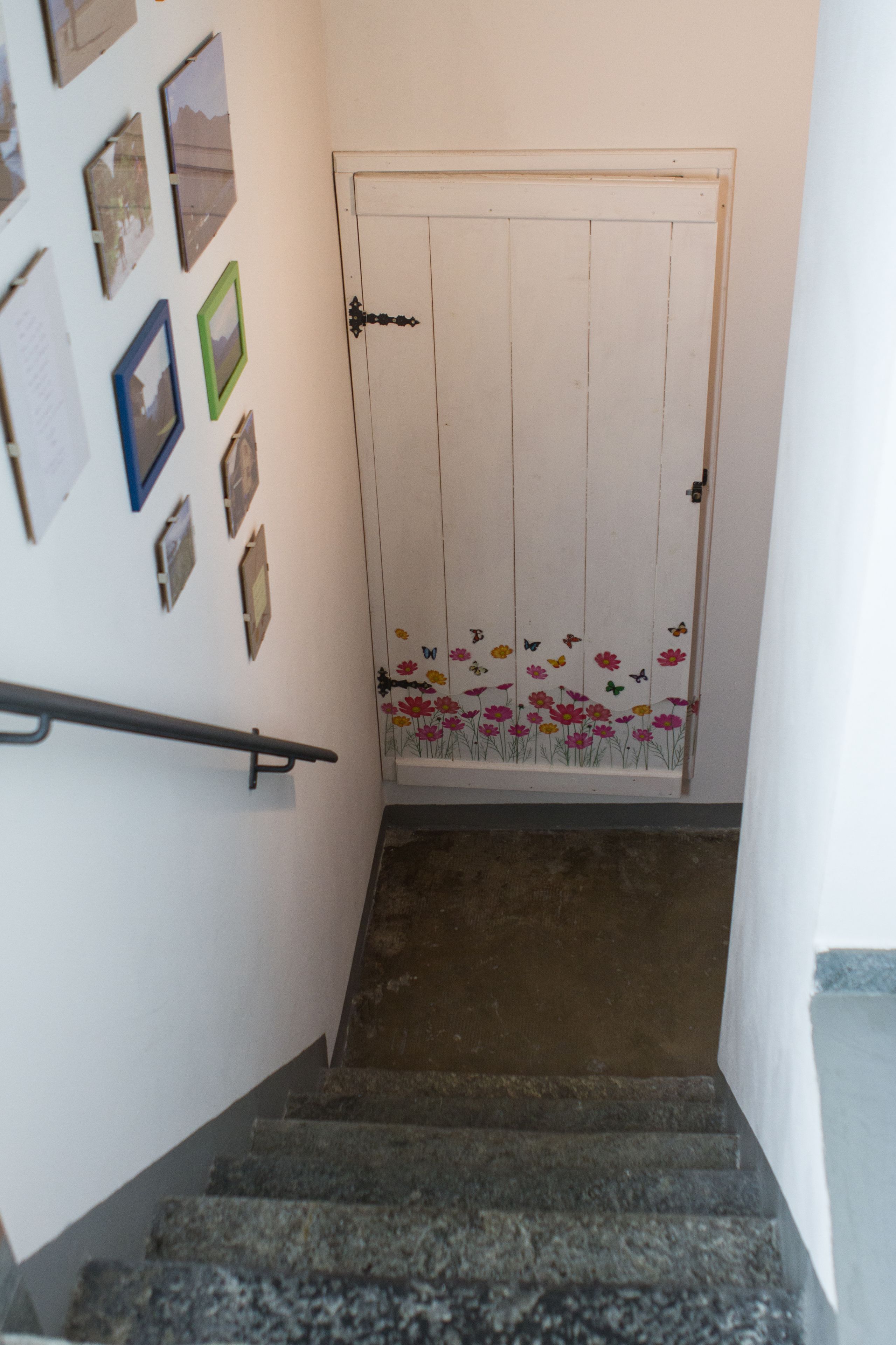 Eine Treppe mit Handlauf, eine Tür mit floralem Dekor und verschiedene Bilderrahmen an der Wand.