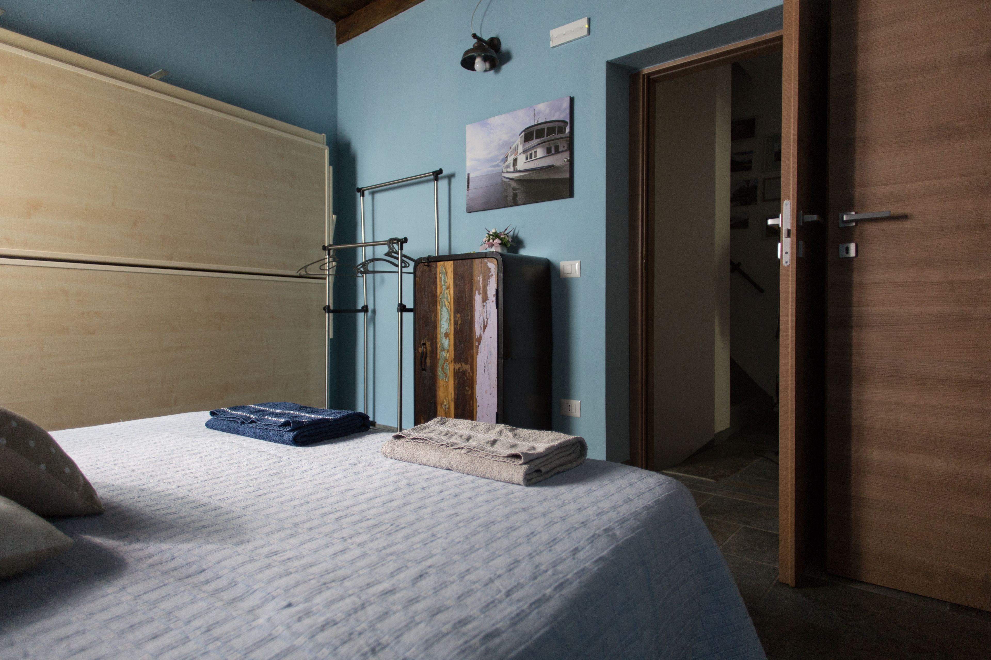 Ein Schlafzimmer mit Bett, Koffer, Handtuch, einer Kleiderstange und einer Tür zu einem weiteren Raum.