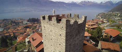 A historic stone tower with a balcony, overlooking a town with red-roofed buildings and a lake.