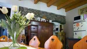 Un comedor con una mesa de madera, sillas con forma de corazón, un jarrón de flores blancas y una pared de piedra.