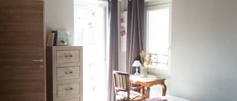 Un dormitorio con cama, cómoda de madera, escritorio con silla y ventana con cortinas.
