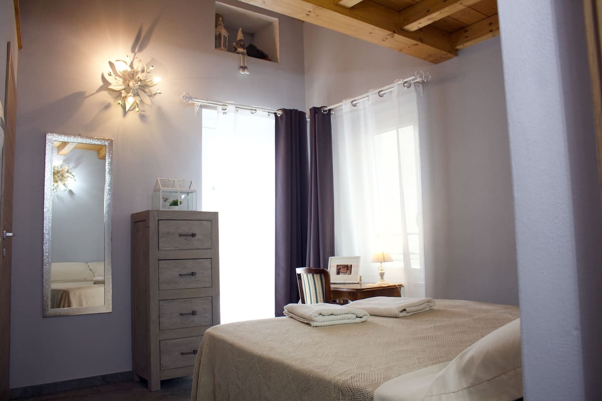A bedroom with a bed, a dresser, a mirror, and a window with curtains.