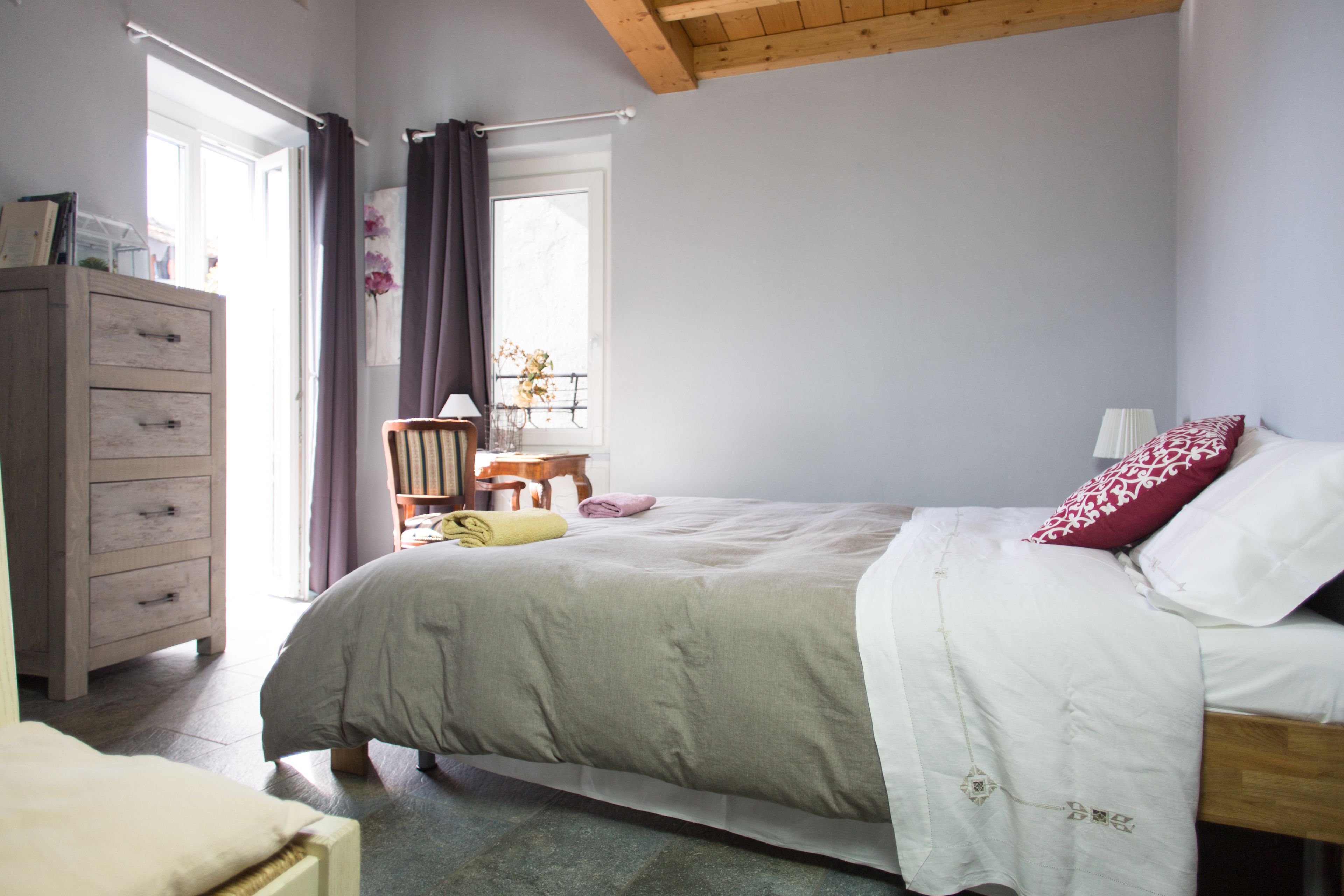 Une chambre à coucher avec un lit, une commode, une fenêtre avec des rideaux et un plafond en bois.
