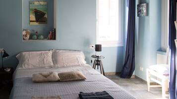 A bedroom with a large bed, a small table, a window with curtains, and a ceiling with exposed beams.