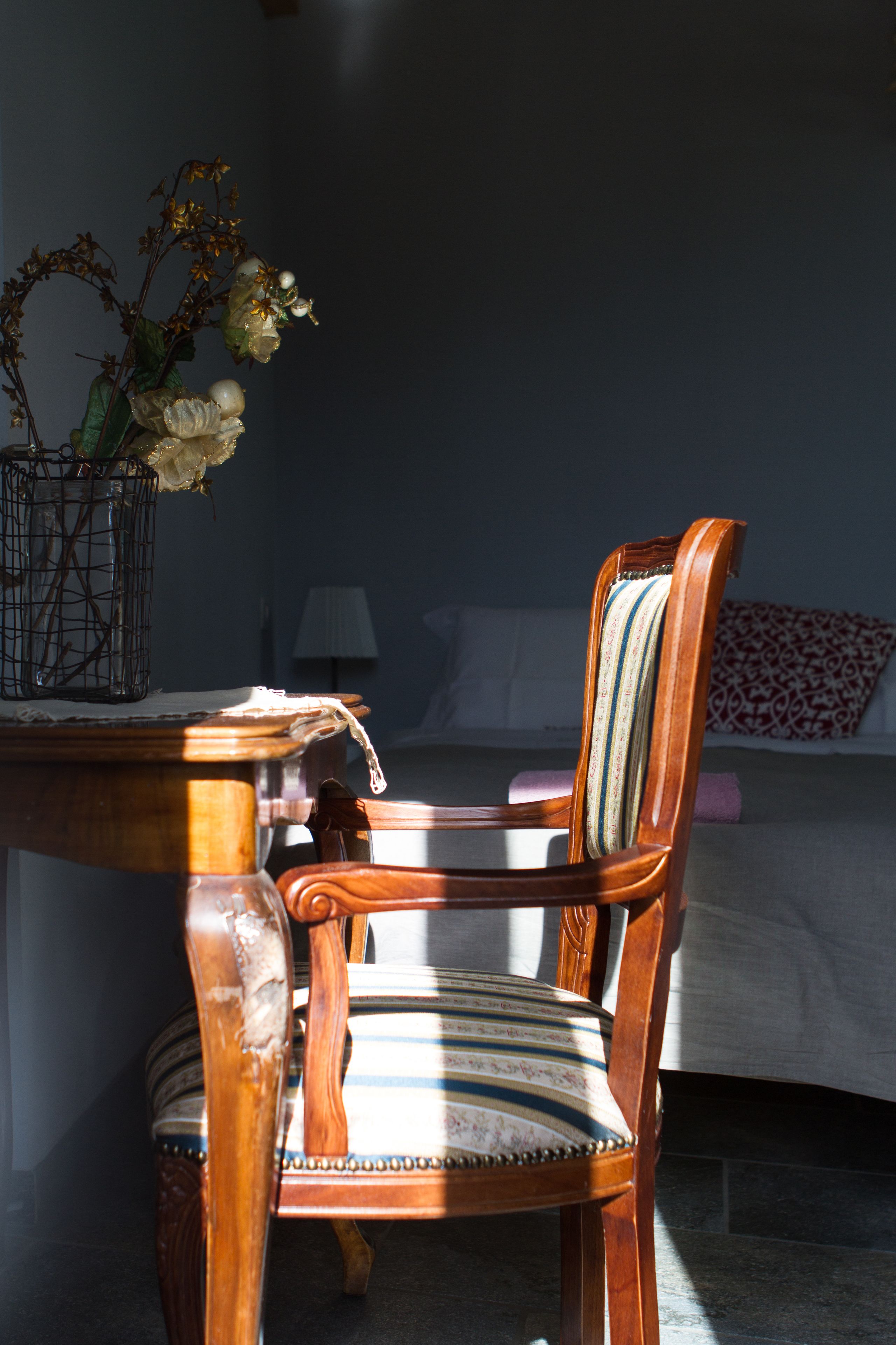 A wooden chair with a striped cushion and a vase with flowers on a table.