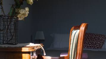 A wooden chair with a striped cushion and a vase with flowers on a table.