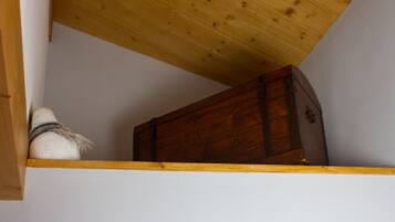 Un cofre de madera en un rincón, con una pared blanca y un techo inclinado.