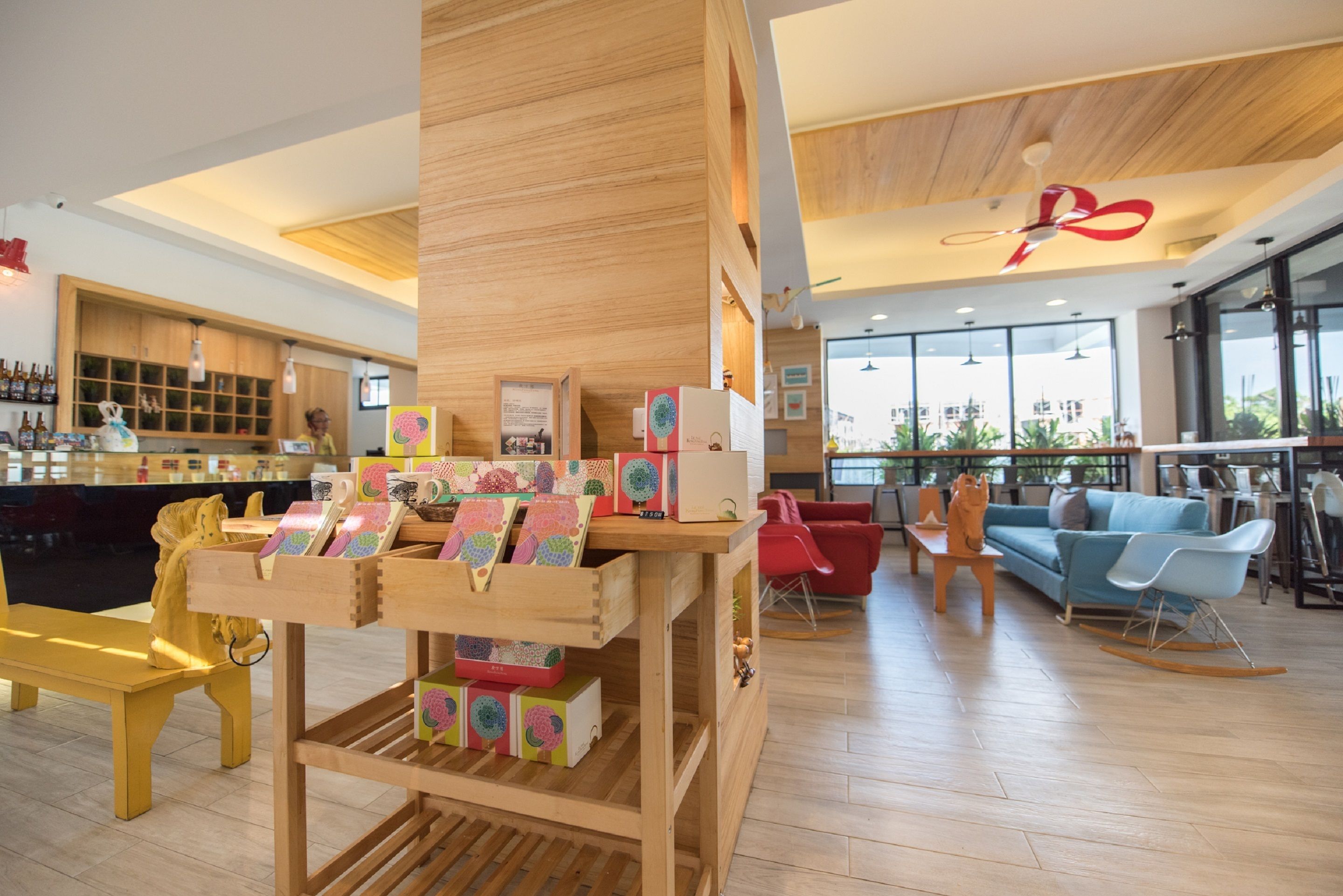 A modern interior with a wooden reception desk, colorful children's books, a bar area, and a seating area with red and blue chairs.