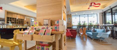A modern interior with a wooden reception desk, colorful children's books, a bar area, and a seating area with red and blue chairs.