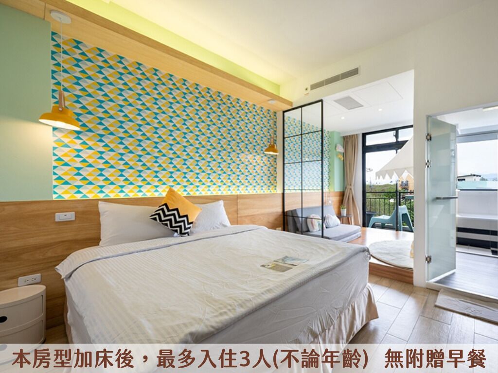 A modern hotel room with a large bed, a patterned wall, and a balcony with outdoor furniture.
