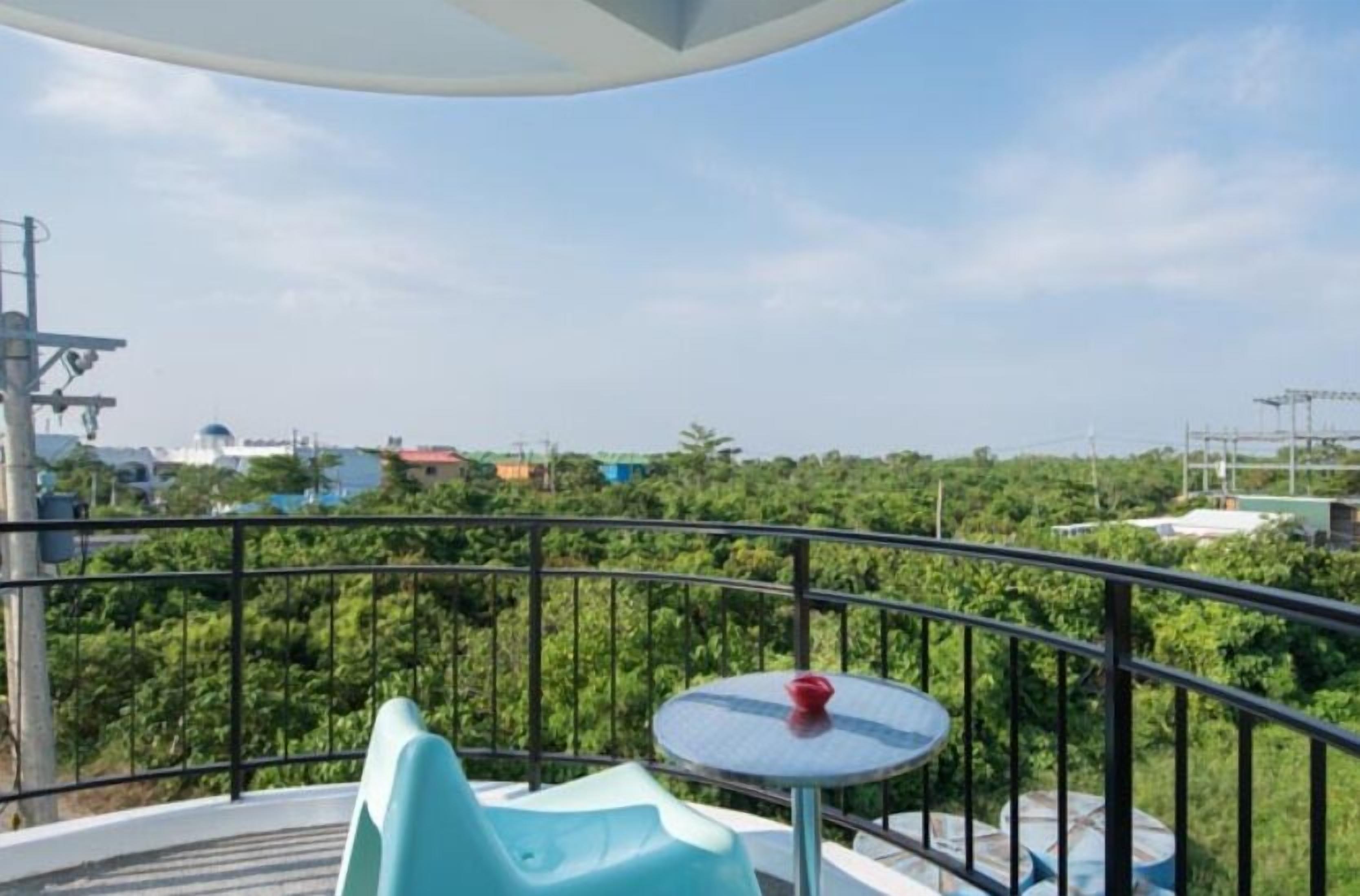 A balcony with a table and chairs, overlooking a lush green landscape and buildings in the distance.