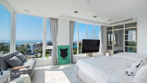 Une chambre d’hôtel moderne dotée d’un grand lit, d’un canapé, d’une télévision et offrant une vue sur l’océan.