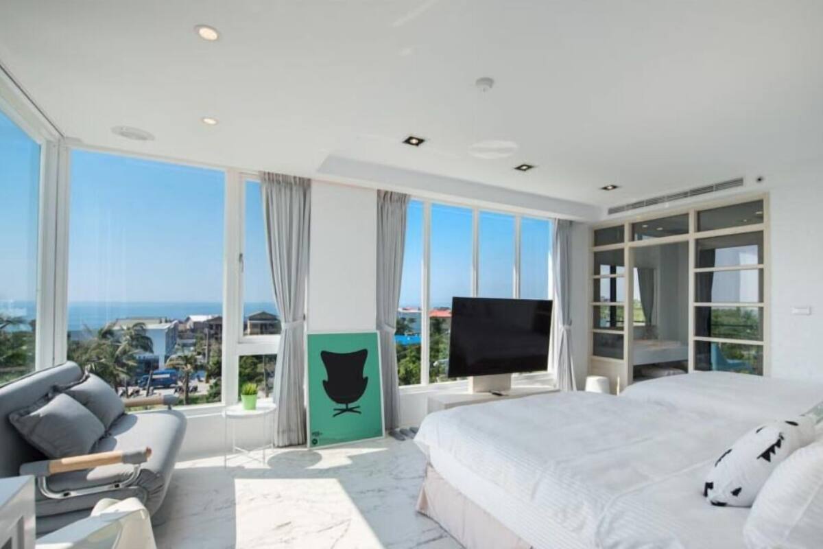 A modern hotel room with a large bed, a sofa, a TV, and a view of the ocean.