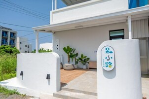 Un edificio moderno con fachada blanca, un área de entrada cubierta con plantas y un cartel con caracteres japoneses.