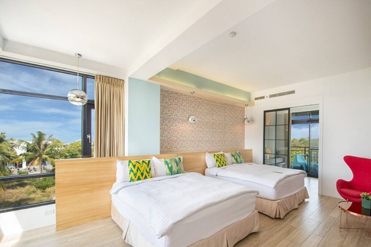 A modern hotel room with two beds, a large window with a view, and a red chair.