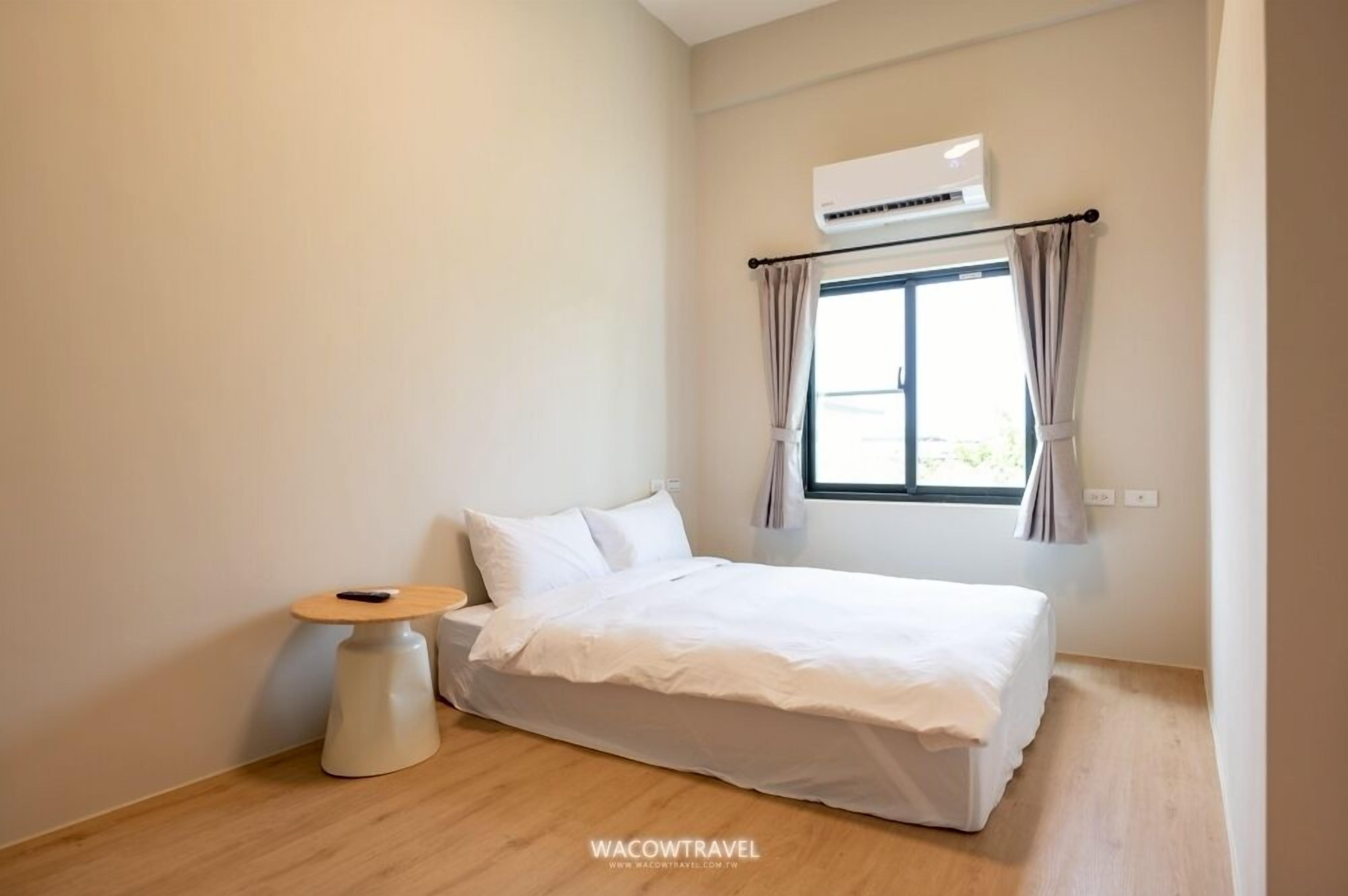 Een minimalistisch ingerichte slaapkamer met een eenpersoonsbed, een klein rond tafeltje en een raam met gordijnen.