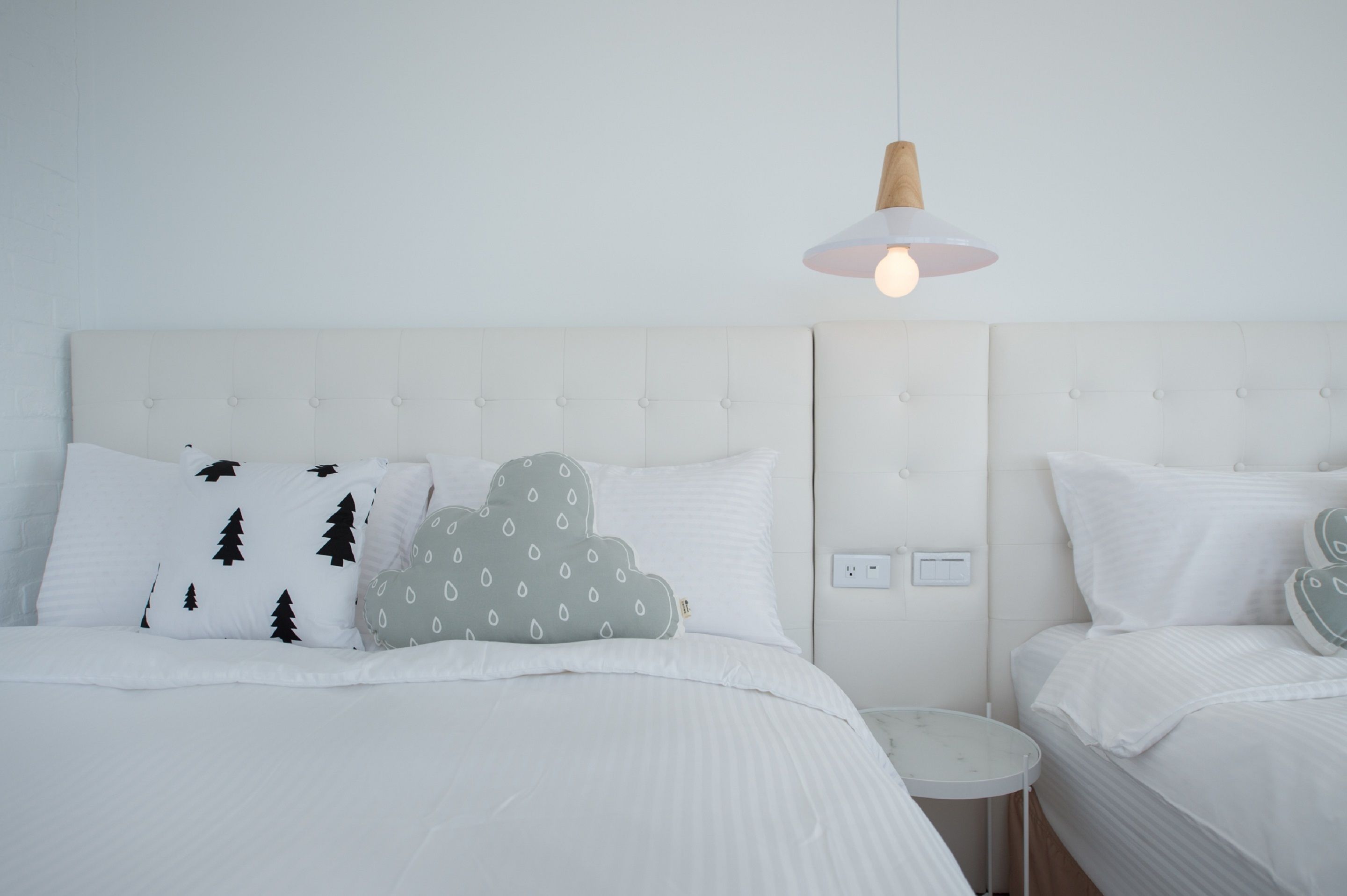 A neatly made bed with white bedding and decorative pillows, a bedside table, and a hanging light fixture.