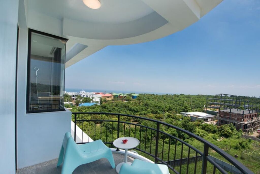 A balcony with a view of a green landscape and buildings in the distance.