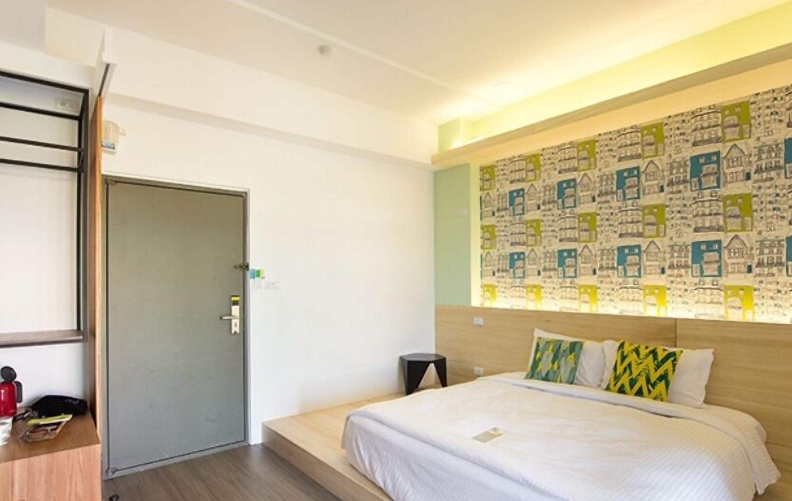 A hotel room with a bed, a desk, a chair, and a door.