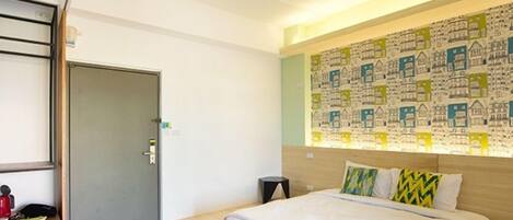 A hotel room with a bed, a desk, a chair, and a door.