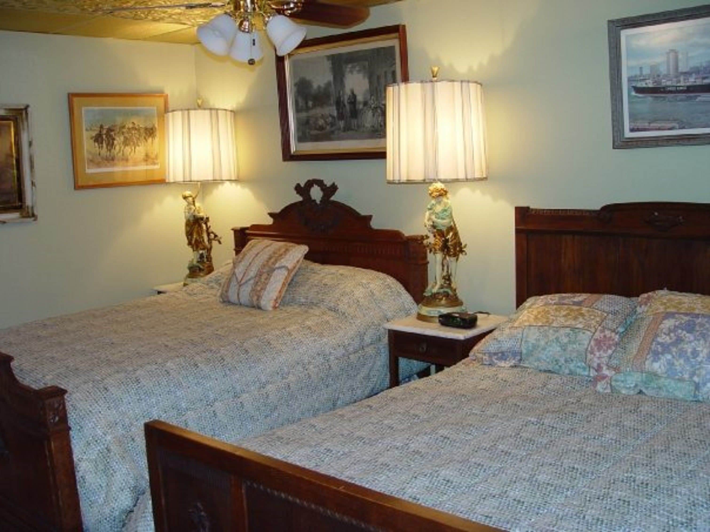 Un dormitorio con dos camas, cada una con cabecera de madera, mesita de noche y lámpara. Hay cuadros en la pared.