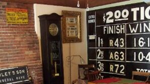 A restaurant interior with a chalkboard displaying a score table, wooden tables and chairs, and a vintage clock. - Old Winterport Commercial House (Winterport)