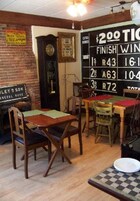Interior de un restaurante con una pizarra mostrando una tabla de puntajes, mesas y sillas de madera, y un reloj antiguo.