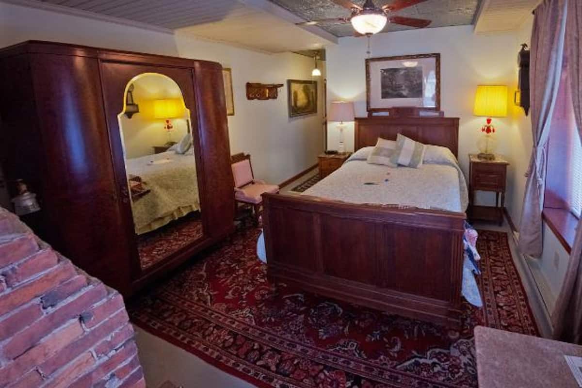 A traditional bedroom with a four-poster bed, a large mirror, and a red patterned rug.