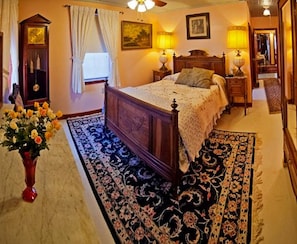 A bedroom with a large bed, a wooden wardrobe, a nightstand, a lamp, a painting on the wall, and a mirror. - Old Winterport Commercial House (Winterport)