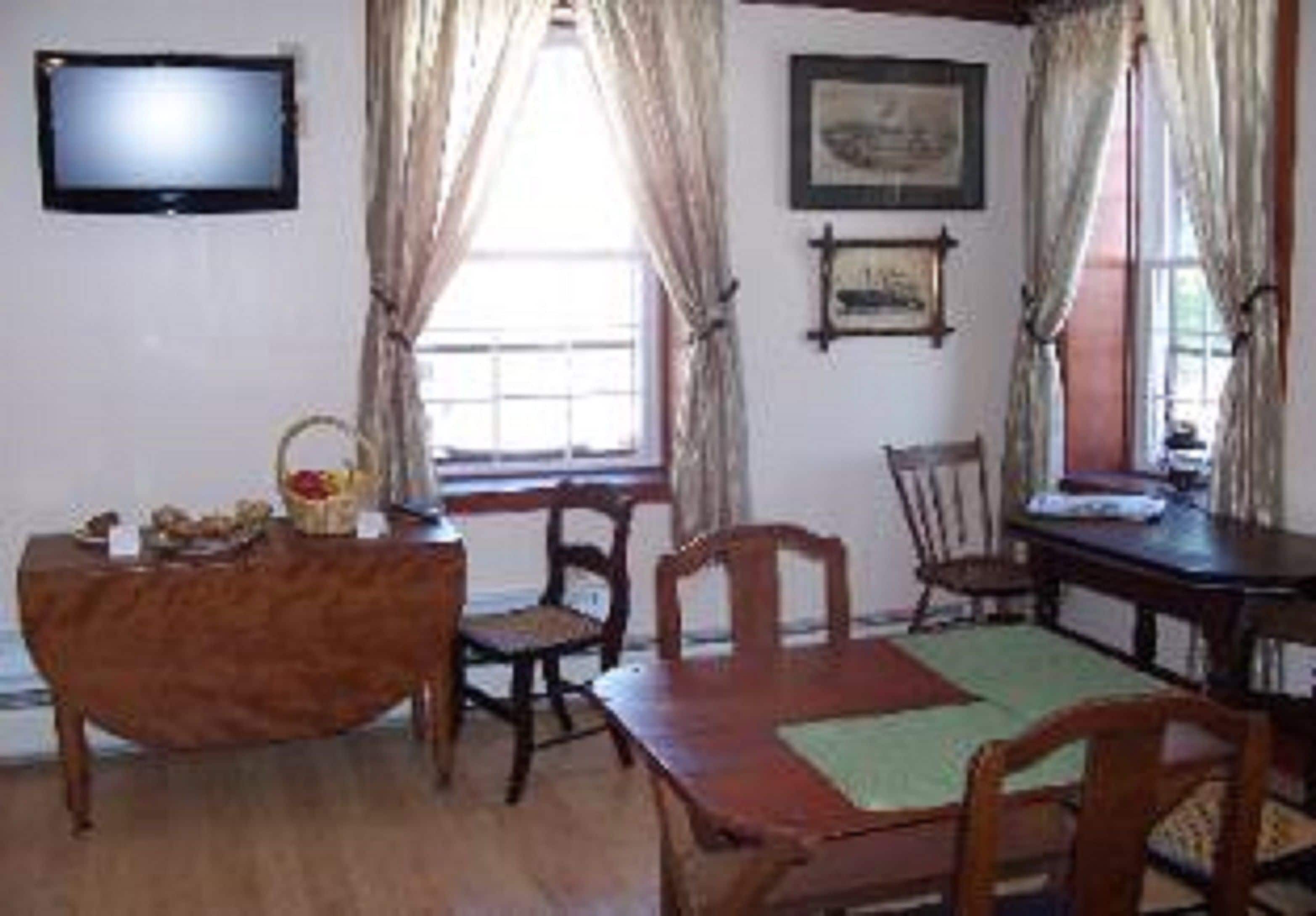 A dining area with wooden furniture, a television mounted on the wall, and windows with curtains.