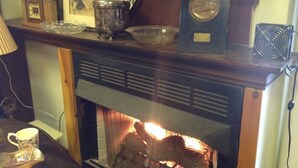 A fireplace with a fire, a clock, and various decorative items on the mantel. - Old Winterport Commercial House (Winterport)