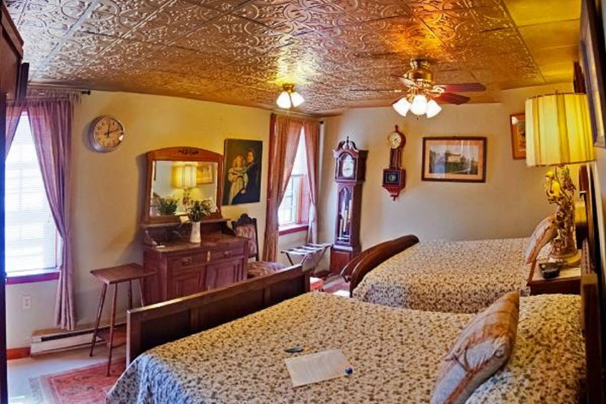 A bedroom with two beds, a dresser, a desk, and a ceiling fan.