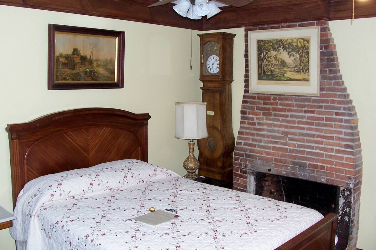 A bedroom with a wooden bed, a clock, a fireplace, and two framed pictures on the wall.