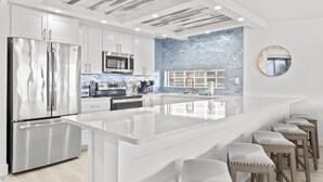 A modern kitchen with white cabinetry, stainless steel appliances, a large island, and a blue-tiled backsplash. - **Newly Remodeled 3/2 Oceanfront ~ 3 King Beds!** (Saint Augustine)