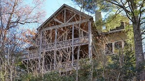 A large, multi-story wooden cabin surrounded by dense forest.