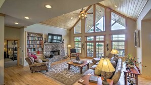 A spacious living room with a fireplace, large windows, and a high ceiling.