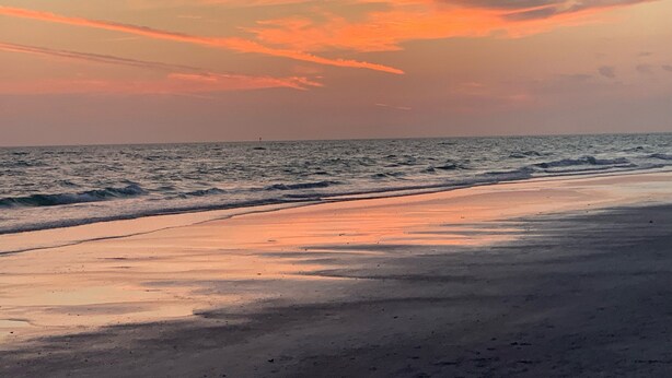 A beach with a sunset, waves, and a distant buoy.