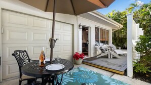 An outdoor patio with a table and chairs, a covered umbrella, and a view of a house with a garage and a deck.