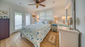 A bedroom with a bed, ceiling fan, bedside tables, lamp, dresser, and a large mirror.