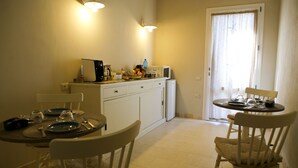 Una cocina pequeña y luminosa con armarios blancos, una mesa de comedor lista con platos, vasos y cubiertos, y dos sillas.