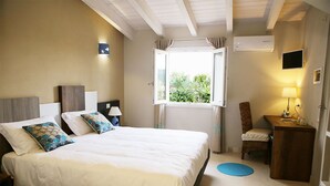 Un dormitorio con cama, mesitas de noche, una silla, un escritorio, una ventana y un equipo de aire acondicionado.