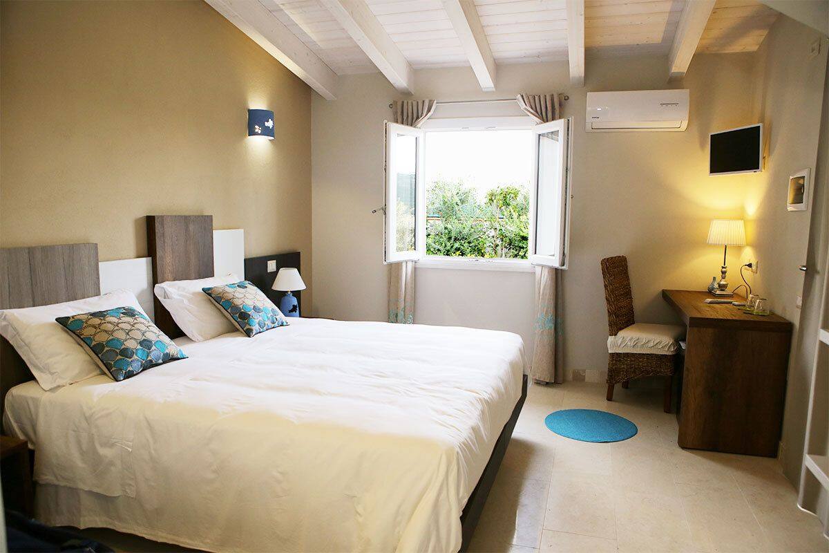 A bedroom with a bed, bedside tables, a chair, a desk, a window, and an air conditioning unit.