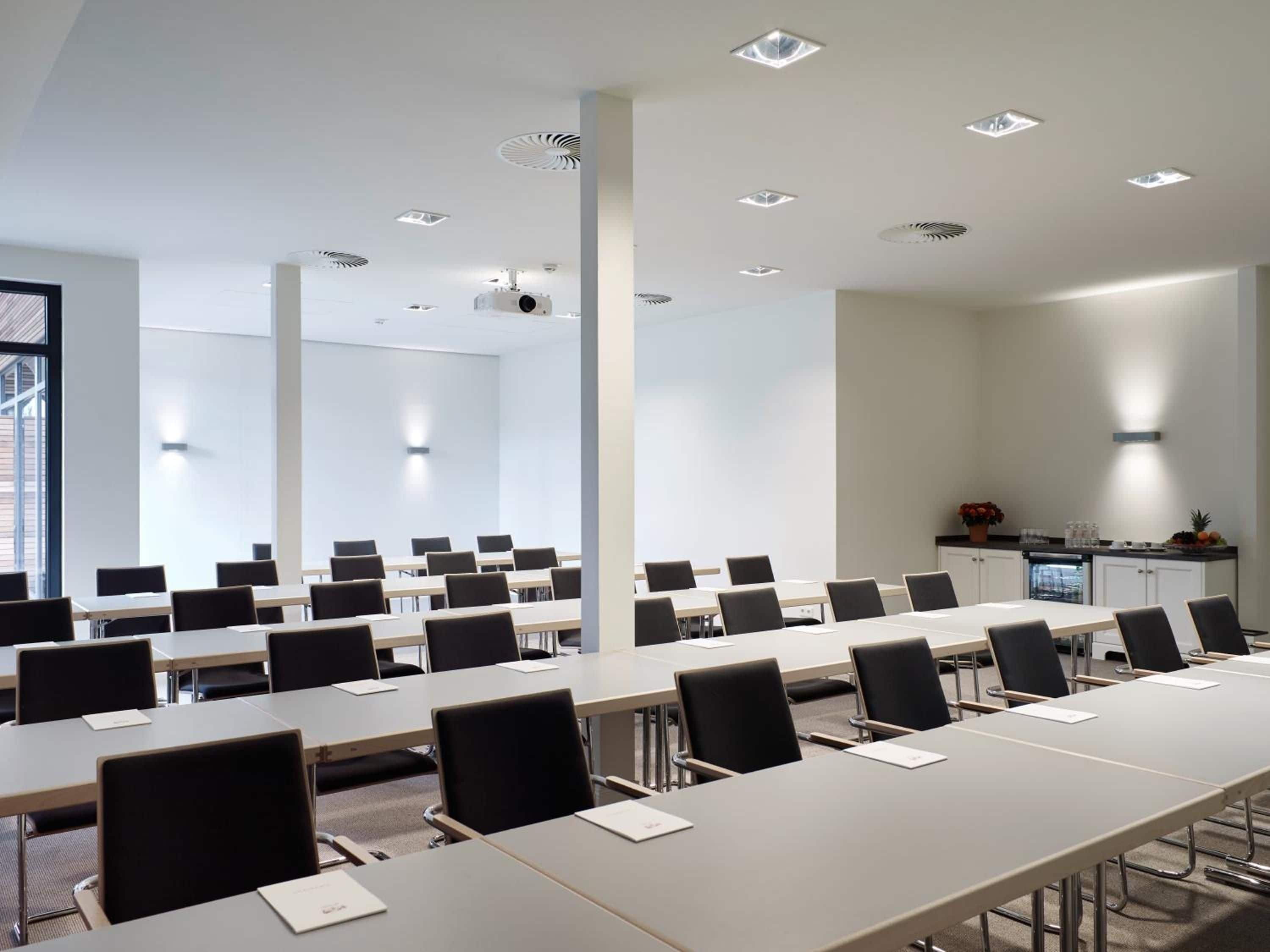A conference room with multiple tables and chairs, a projector, and a kitchenette area.