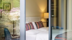 Een hotelkamer met een bed, een stoel en een raam met uitzicht op bomen en bloemen.