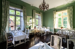 A dining room with multiple tables set for a meal, large windows with curtains, and a chandelier.