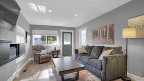 Ein modernes Wohnzimmer mit einem grauen Sofa, einem braunen Ledersessel, einem Holztisch und einem Bild an der Wand.