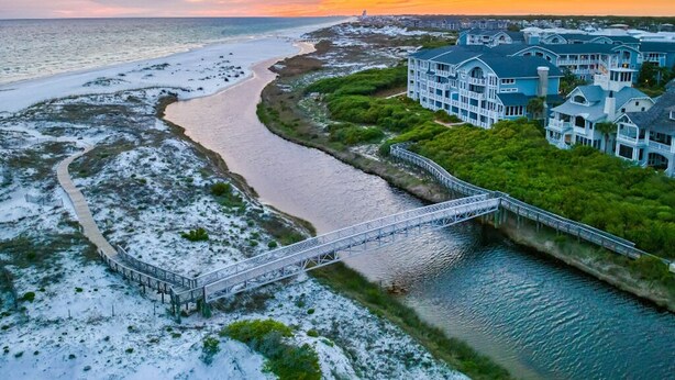 A coastal property with a bridge over a river, surrounded by lush greenery and a beach.